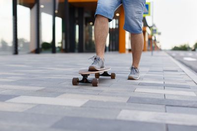 Photo of men skateboarding in city with one foot placed on board and pushing off with the other