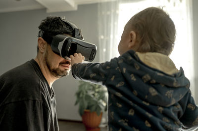 Baby boy looking at father wearing virtual reality simulator at home