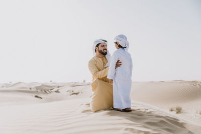 Couple kissing on sand against clear sky