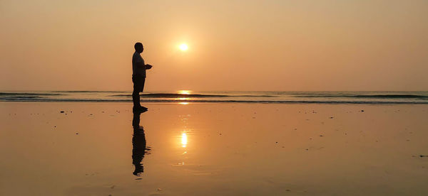 Silhouette man standing on beach during sunset