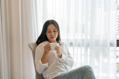 Young woman using phone while sitting on bed at home