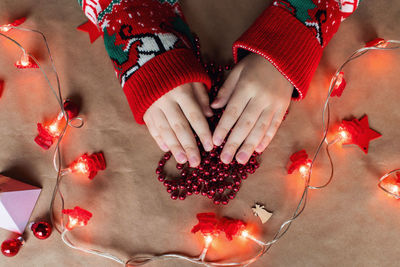 A red christmas garland in children's hands lies on the table