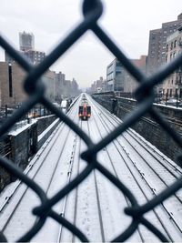 Train passing above snow covered tracks seen through chainlink fence