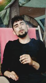 Young man smoking cigarette while sitting outdoors