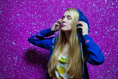 Woman listening music while standing against colored background