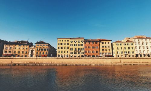 Buildings by river against clear blue sky