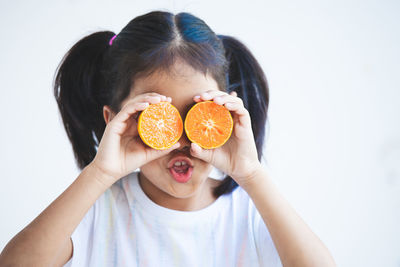 Close-up of girl holding orange slices against white background