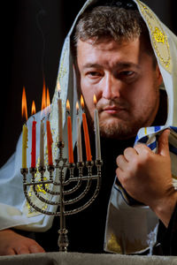 Man with jewish prayer shawl looking at menorah