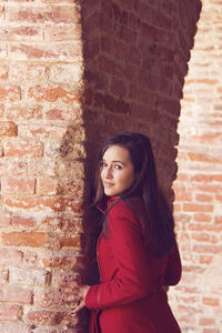 Portrait of beautiful young woman standing against brick wall