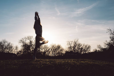 Silhouette woman jumping on field against sky during sunset