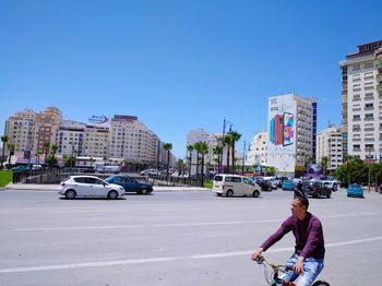 Man riding motorcycle on street in city against clear sky