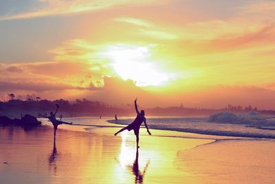 Playful men at beach against sky during sunset