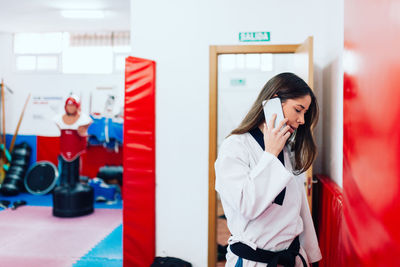 Young woman using phone while standing on mirror