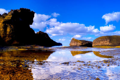 Reflection of rocks in sea against blue sky