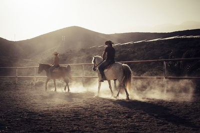 Man and woman riding horses on field against mountain