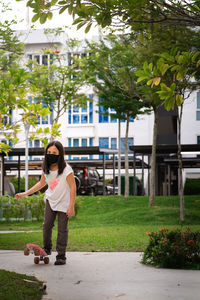 Young girl wearing reusable black face mask skateboarding in the park.