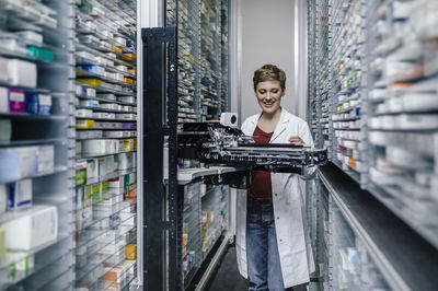 Smiling pharmacist with commissioning machine in pharmacy