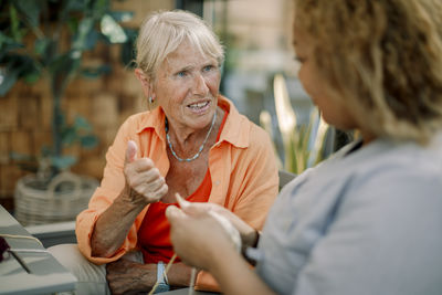 Elderly woman talking with young female nurse at retirement home