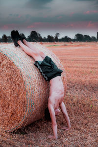 Shirtless teenage boy doing handstand by hay bale at farm