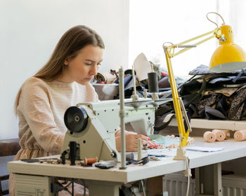 Young focused woman seamstress sewing clothes with sewing machine while working in fashion workshop