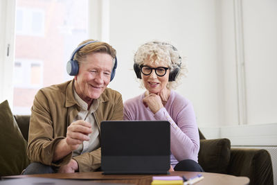 Senior man and woman sitting in living room and using digital tablet to edit podcast