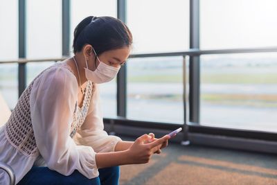 Woman using mobile phone while sitting on window