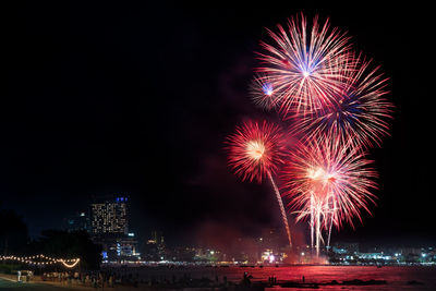 Firework display over illuminated city against sky at night