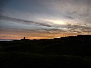 Silhouette man on field against sky during sunset