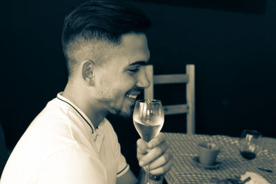 Side view of smiling young man having wine at table in restaurant
