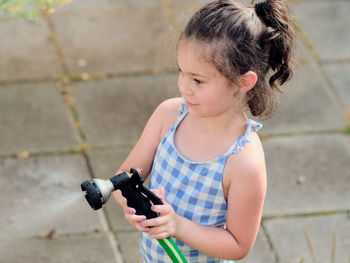 Young girl is watering plants in the backyard while wearing a bathing suit