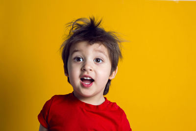 Cheerful baby boy in red t-shirt stands on yellow background