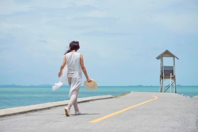 Rear view of man standing on road by sea against sky