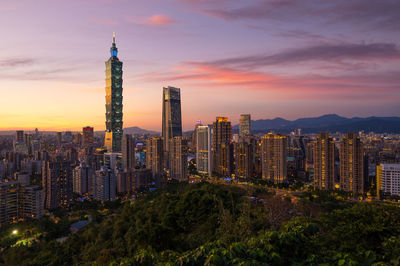 Illuminated buildings in city against sky during sunset