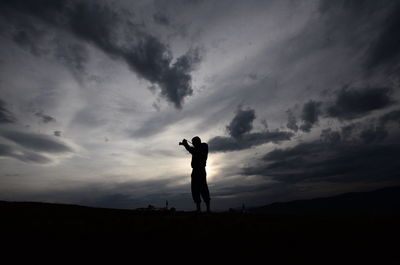 Silhouette woman photographing against sky during sunset