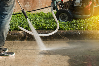 Low section of man standing spraying water on footpath