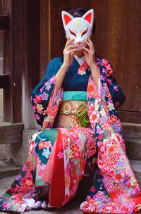 Woman wearing traditional clothing and mask against door