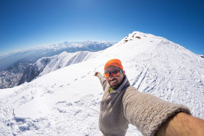 Portrait of man standing on snow covered mountain against clear sky