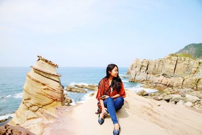 Young woman on rock by sea against sky