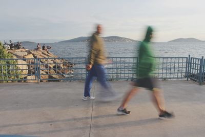 People walking by sea in city against sky