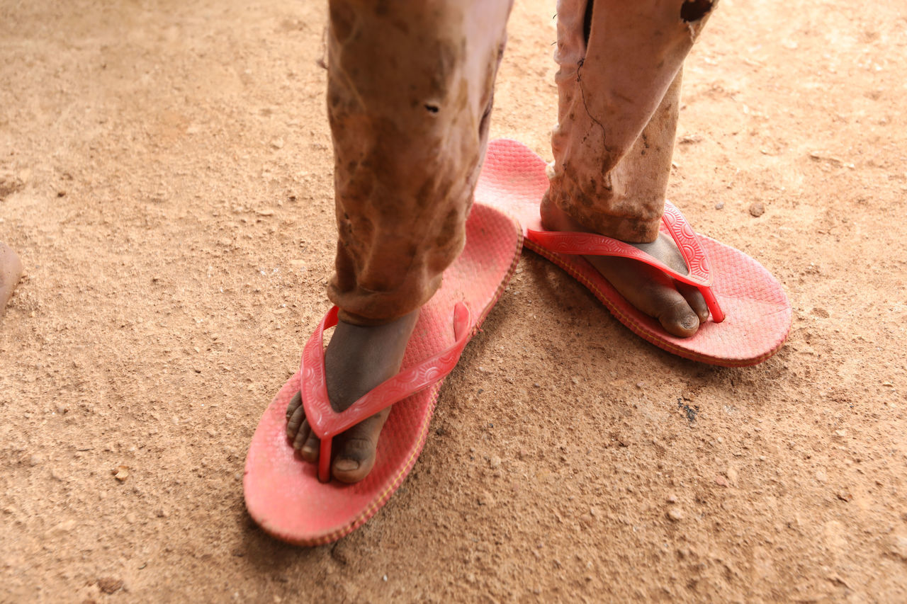 LOW SECTION OF PERSON WEARING RED SHOES STANDING ON SAND