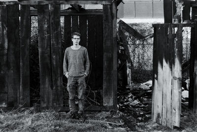 Portrait of young man standing by abandoned wooden structure