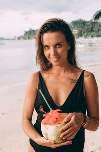 Portrait of smiling woman holding ice cream on beach