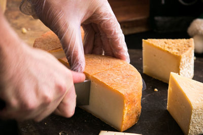 Cropped hands cutting cheese on table