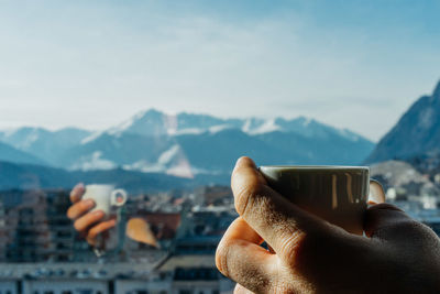 Cropped hand holding coffee cup at glass window