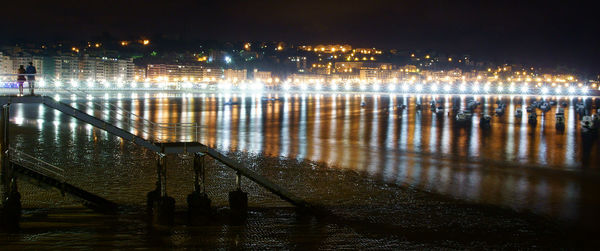 Illuminated city by river against sky at night