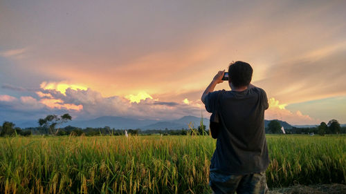 Man standing in field against sky during sunset