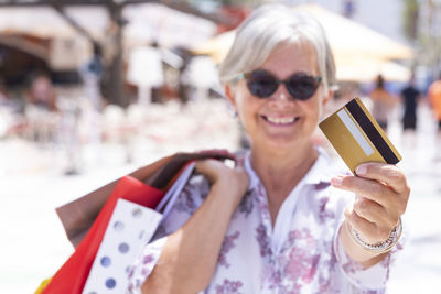 Portrait of smiling senior woman holding credit card outdoors