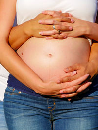 Midsection of pregnant couple touching abdomen