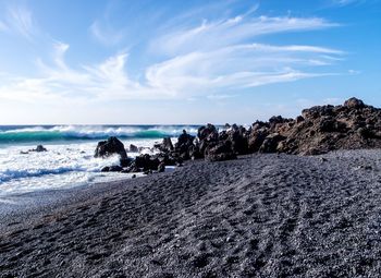 Scenic view of black sand beach against blue sky