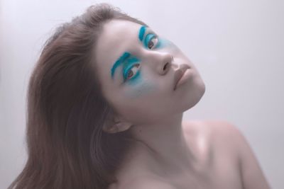 Close-up portrait of young woman with make-up against white background